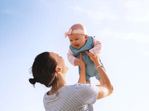 Mamá alzando su bebé al aire libre, ambos riendo. Concepto de bebé saludable.