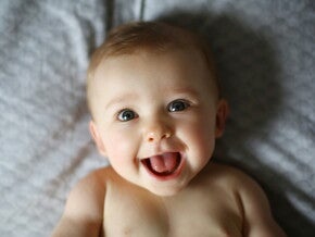 Bebé de 6 meses acostado en la cama sonriendo.