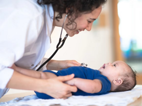 Bebé acostado en cama mientras la doctora le revisa y sonríe.