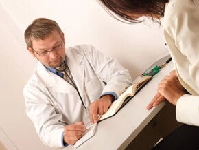 Mujer embarazada en una consulta con su profesional de la salud recetándole ácido fólico.