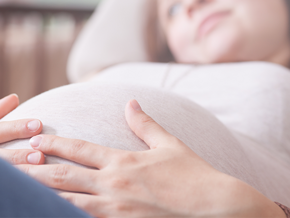 Mujer embarazada acostada y acariciando su vientre.
