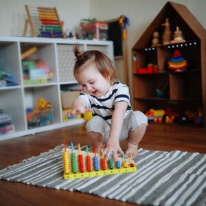 Niña de dos años jugando sobre la alfombra con ábaco de madera. Juego tranquilo como rutina diaria.