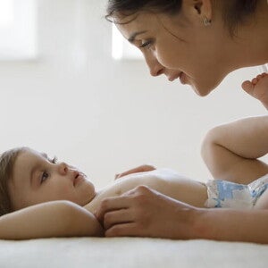 Bebé acostado boca para arriba en pañales, manos de mamá lo acarician