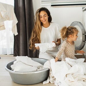 Fomentar la responsabilidad en los niños Madre e hija al lado de un lavarropas, con ropa blanca alrededor para fomentar responsabilidad en los niños