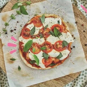 Pizza margarita en el centro con decoración de queso y albahaca alrededor