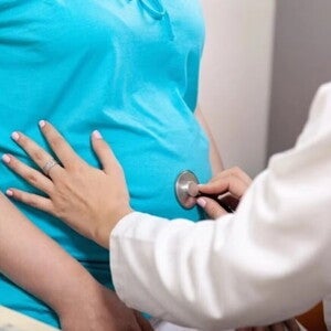 Doctora con un estetocopio por el vientre de una mujer embarazada.