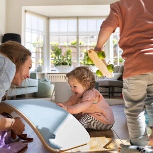 Tiempo de calidad con sobrinos Mujer adulta y dos niños juegan en una sala, con un tablero de equilibrio y un coche de juguete.
