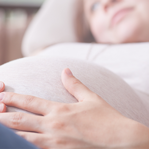 Mujer embarazada acostada y acariciando su vientre.