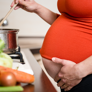Mujer embarazada parada en frente de la cocina, preparando comida con ácidos grasos esenciales.