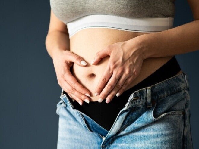 Abdomen de persona embarazada en primer o segundo trimestre, manos en forma de corazón sobre el vientre.
