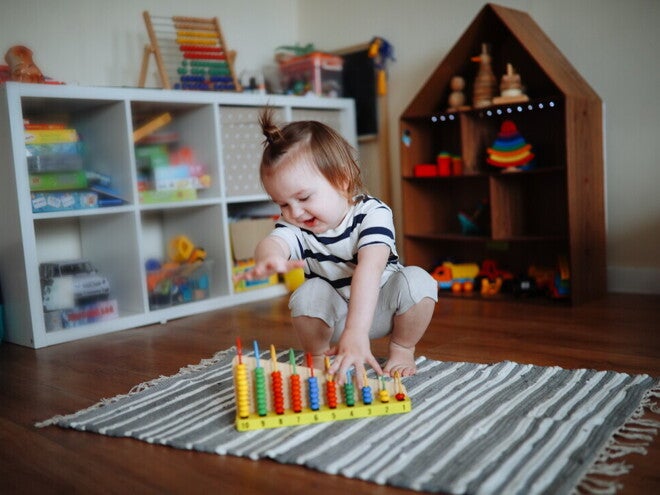 Niña de dos años jugando sobre la alfombra con ábaco de madera. Juego tranquilo como rutina diaria.