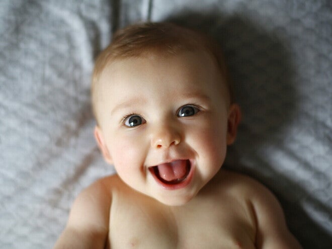 Bebé de 6 meses acostado en la cama sonriendo.