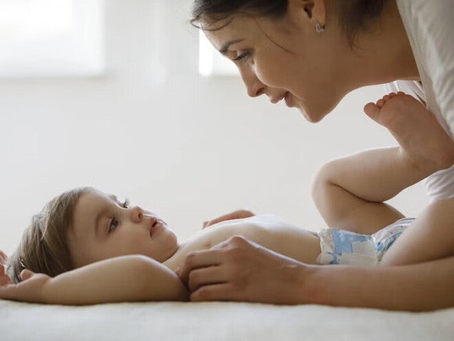 Bebé acostado boca para arriba en pañales, manos de mamá lo acarician