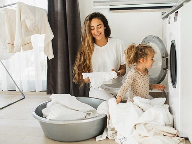 Fomentar la responsabilidad en los niños Madre e hija al lado de un lavarropas, con ropa blanca alrededor para fomentar responsabilidad en los niños