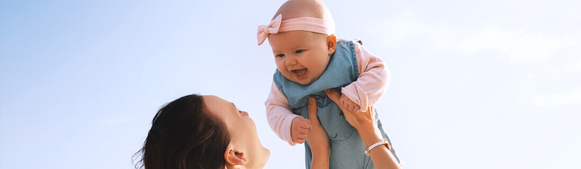 Mamá alzando su bebé al aire libre, ambos riendo. Concepto de bebé saludable.
