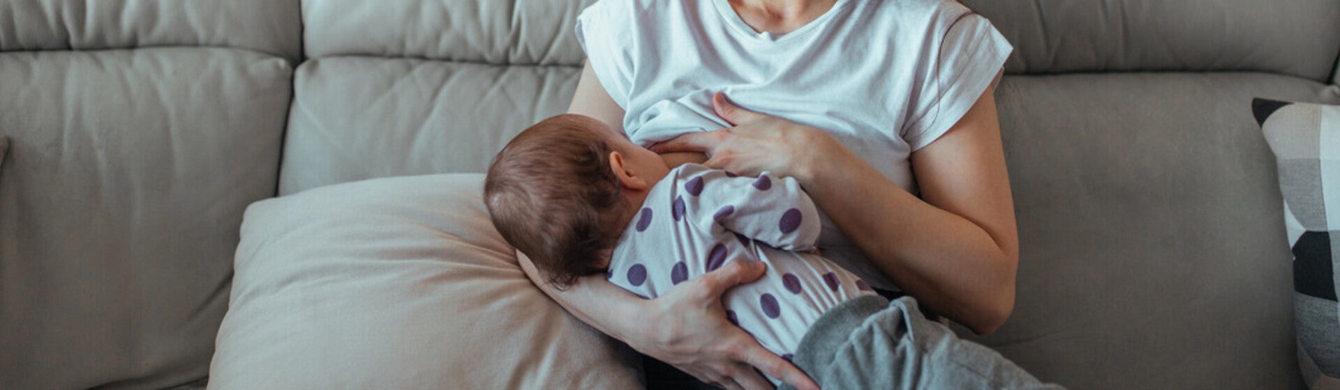 Mamá sentada en un sofá sonriendo, amamantando a su bebé. Lactancia materna.