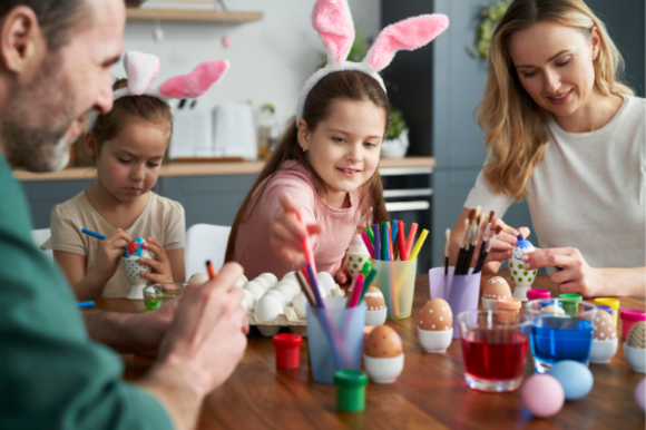Familia de cuatro personas decorando huevos de Pascua en casa.