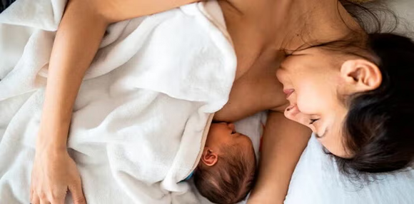 Mamá acostada alimentando a su bebé recién nacido.