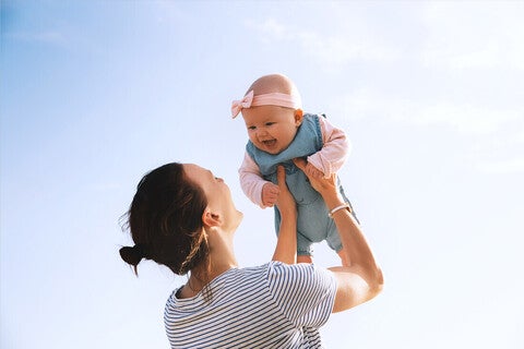 Mamá alzando su bebé al aire libre, ambos riendo. Concepto de bebé saludable.